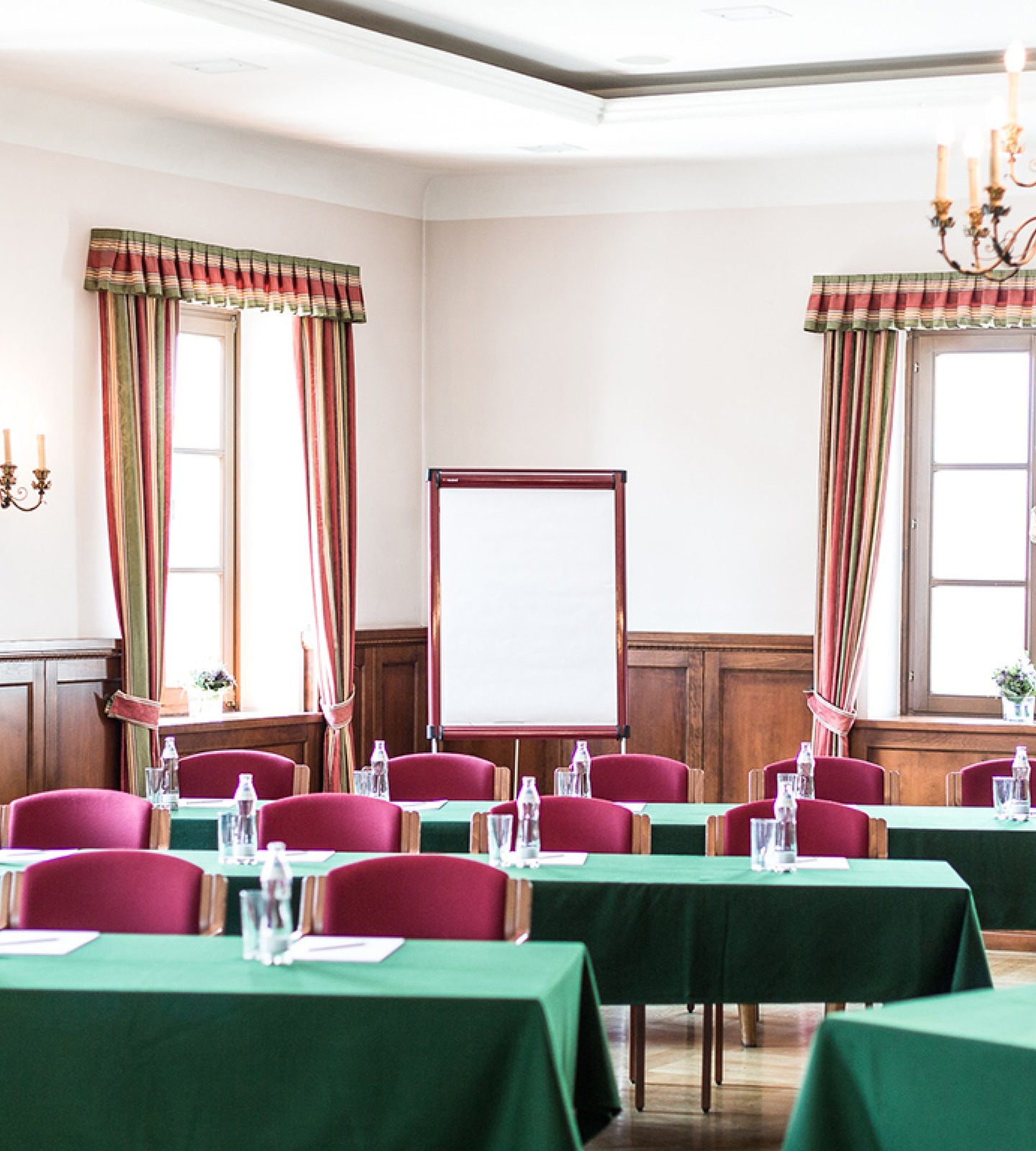 Ein Konferenzraum mit grünen Tischen, roten Stühlen, Vorhängen und einem Flipchart im Hintergrund.