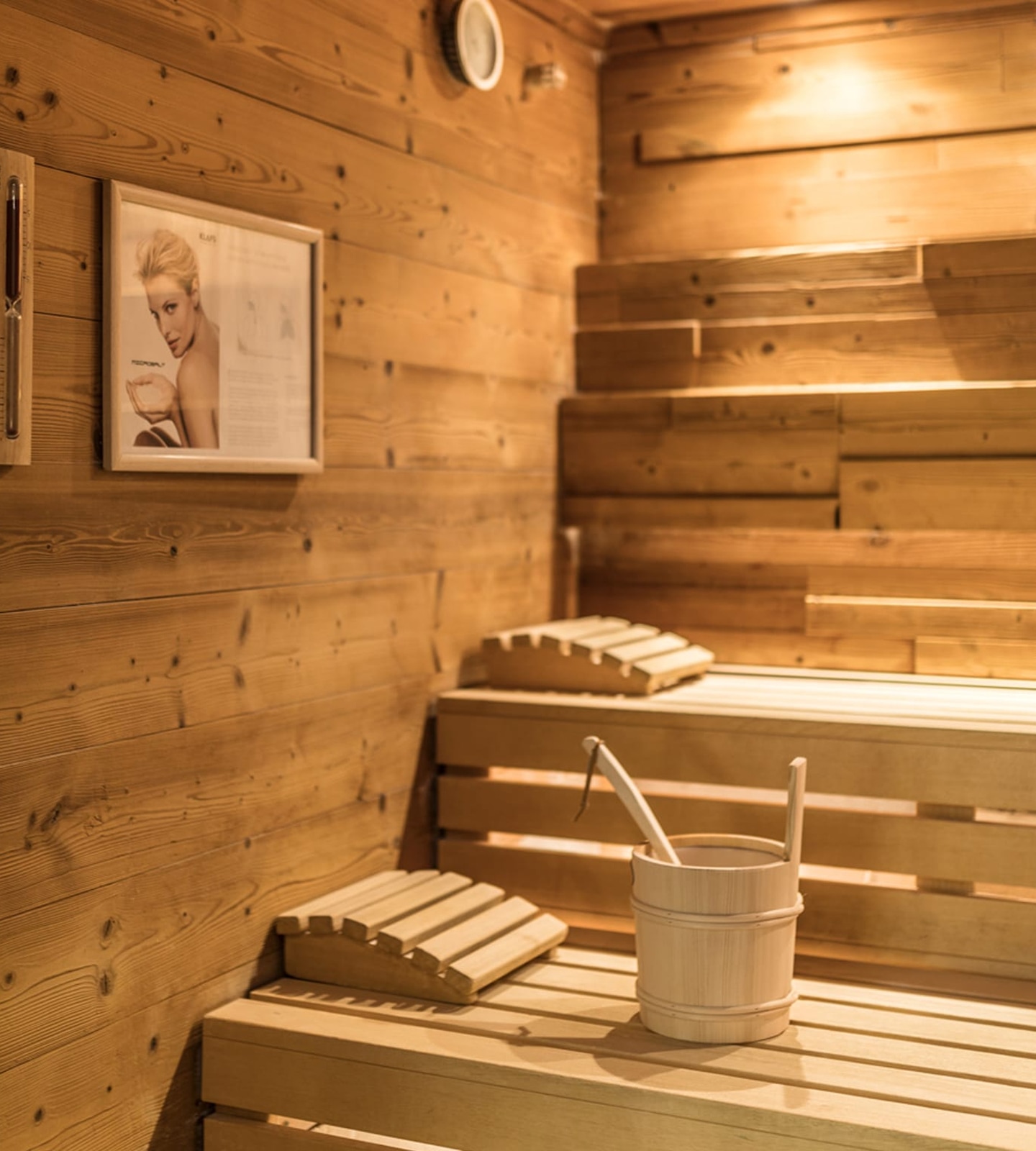 Holzsauna mit Holzkübel, Kelle, Kopfstützen und gemütlicher Beleuchtung.