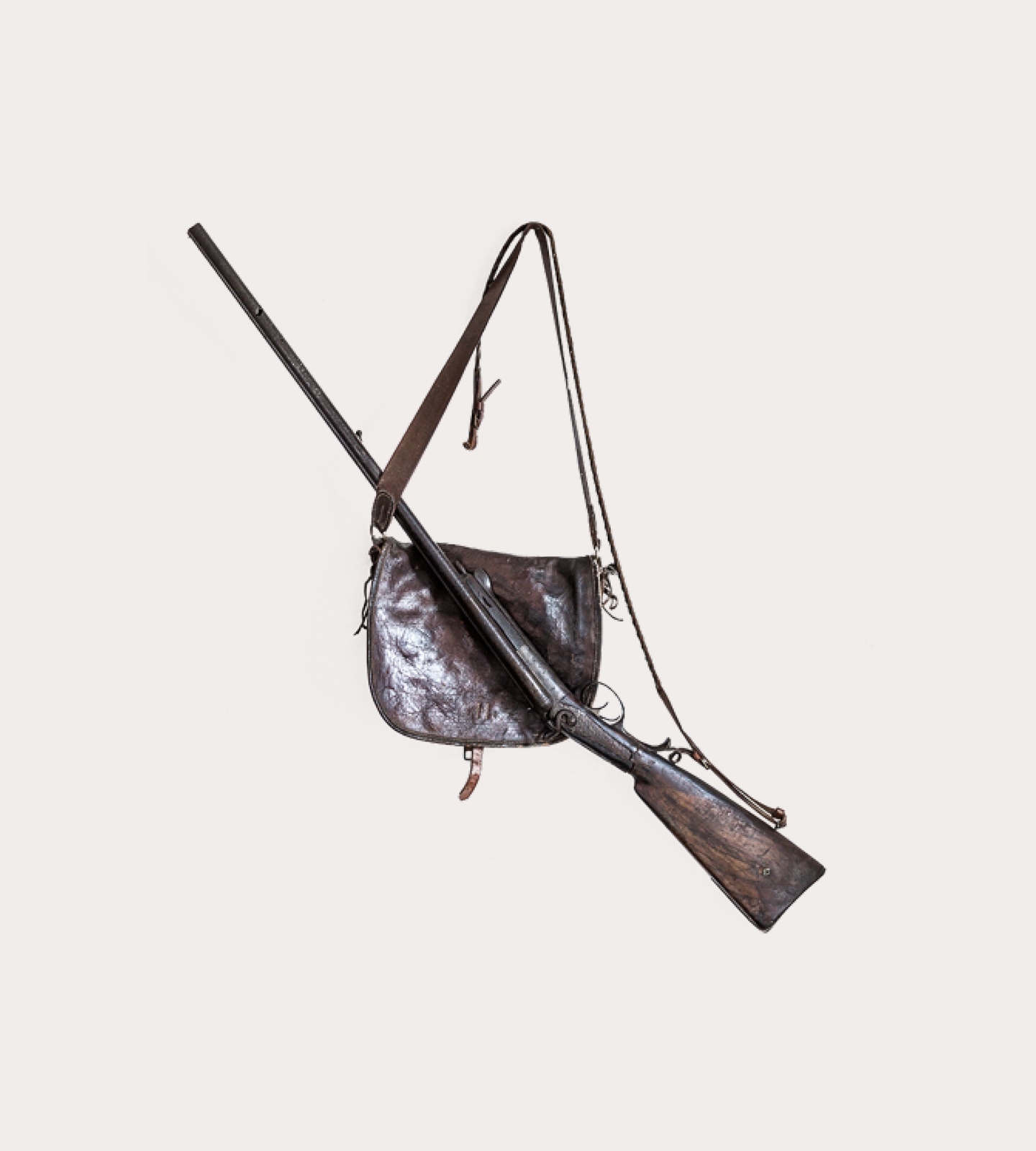 Historisches Gewehr quer über einer alten, abgenutzten Jagdtasche aus braunem Leder vor hellem Hintergrund.