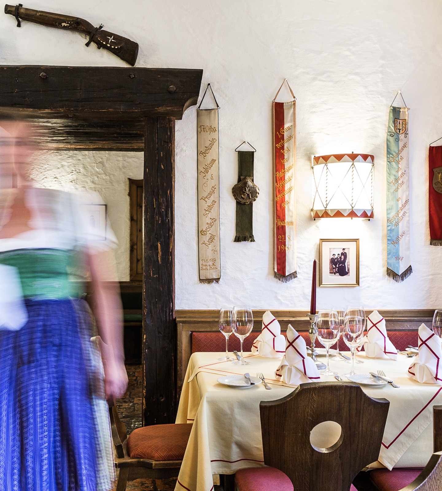 Ein gedeckter Tisch in einer bayerischen Gaststube mit einer Kellnerin in Dirndl in Bewegungsunschärfe.