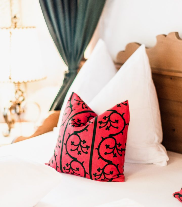 Rustikales Holzbett mit weißen Kissen und roten Zierkissen im Landhausstil.