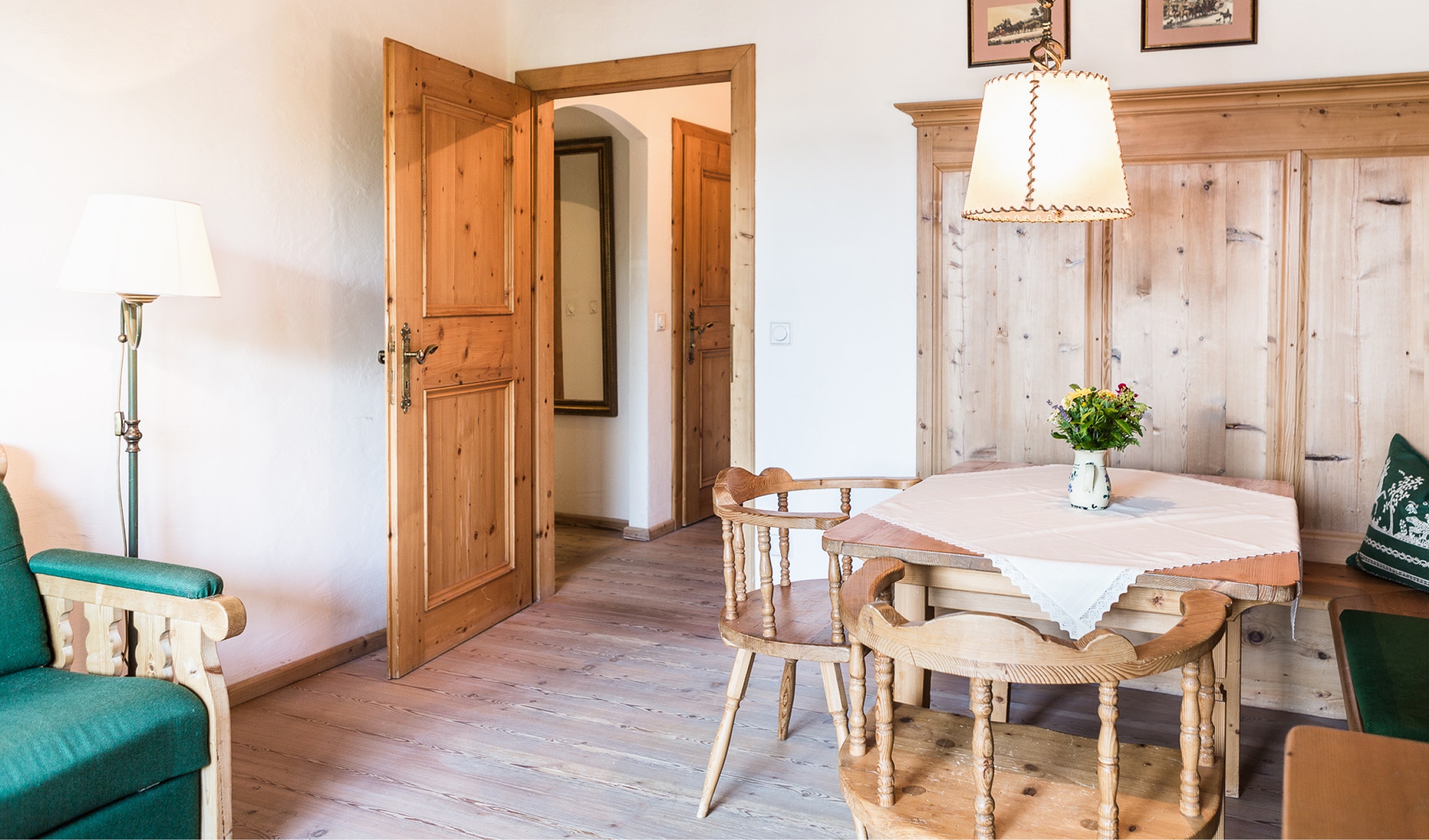 Rustikaler Essbereich aus Holz mit Tisch, Stühlen und hängender Lampe neben einer geöffneten Holztür.