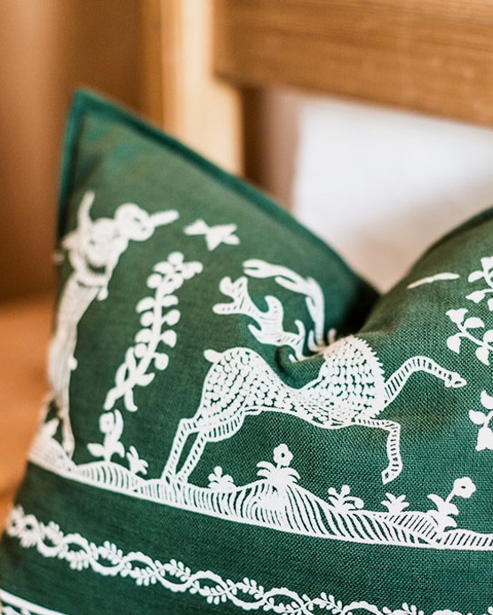 Grünes Kissen mit weißen, traditionell eingestickten Wald- und Tiermotiven, wie einem Hirsch.