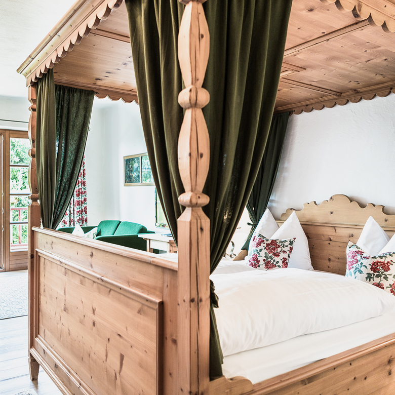 Rustikales Himmelbett aus Holz mit grünen Vorhängen und weißer Bettwäsche im alpinen Stil.