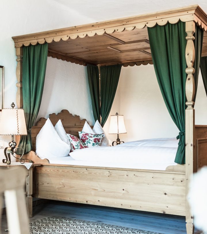 Himmelbett aus hellem Holz mit grünen Vorhängen in einem rustikalen Hotelzimmer mit Fernseher.