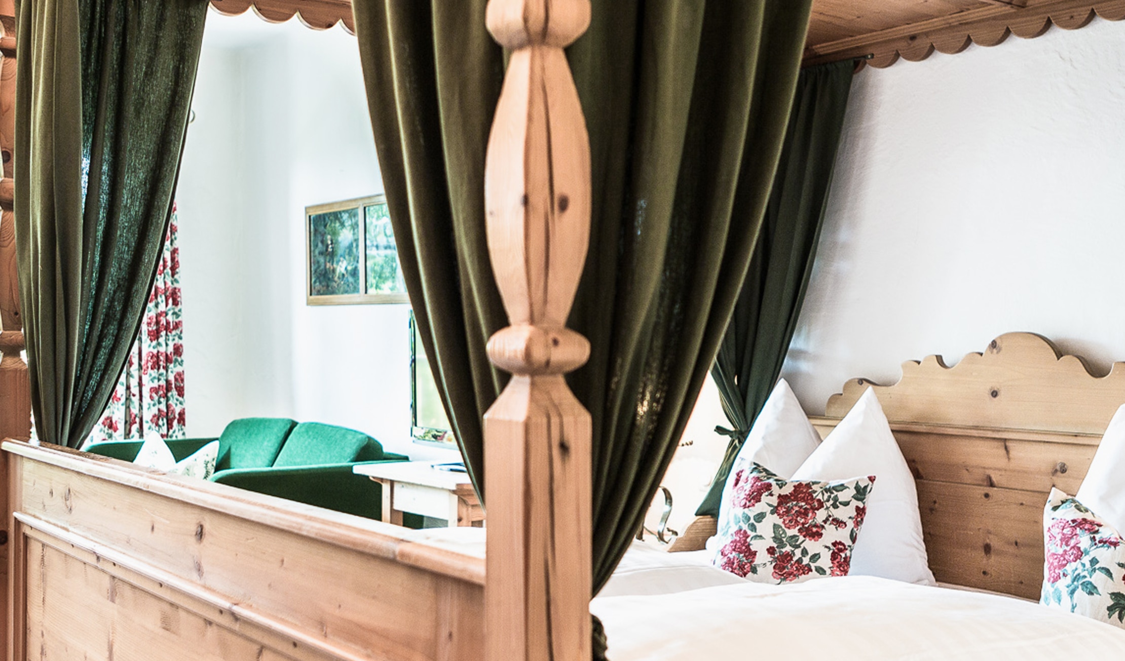Rustikales Himmelbett aus Holz mit grünen Vorhängen, weißen Kissen und floralem Muster in einem Hotelzimmer.