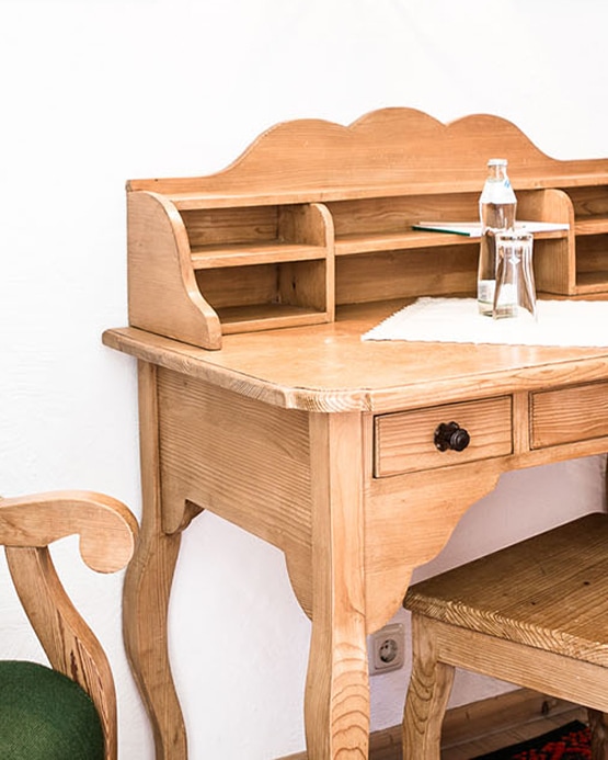 Rustikaler Holzsekretär mit Schubladen, Aufsatzregal, einer Flasche Wasser und Glas auf weißem Hintergrund.