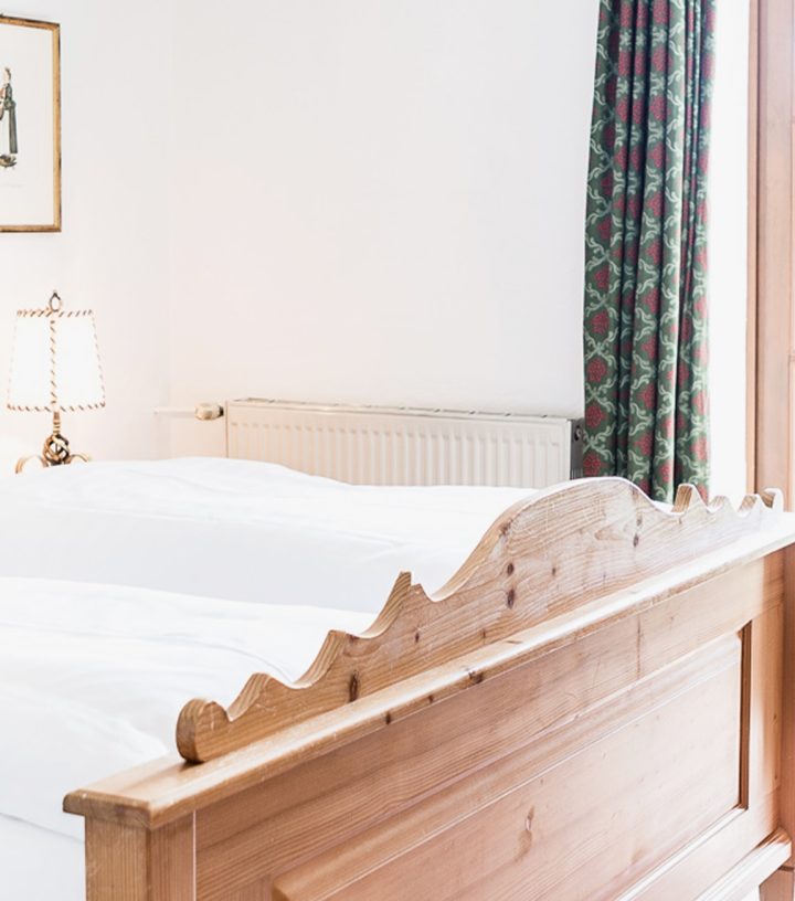 Helles Schlafzimmer mit traditionellem Holzdoppelbett, roten Dekokissen und Balkontür im Gutshof.