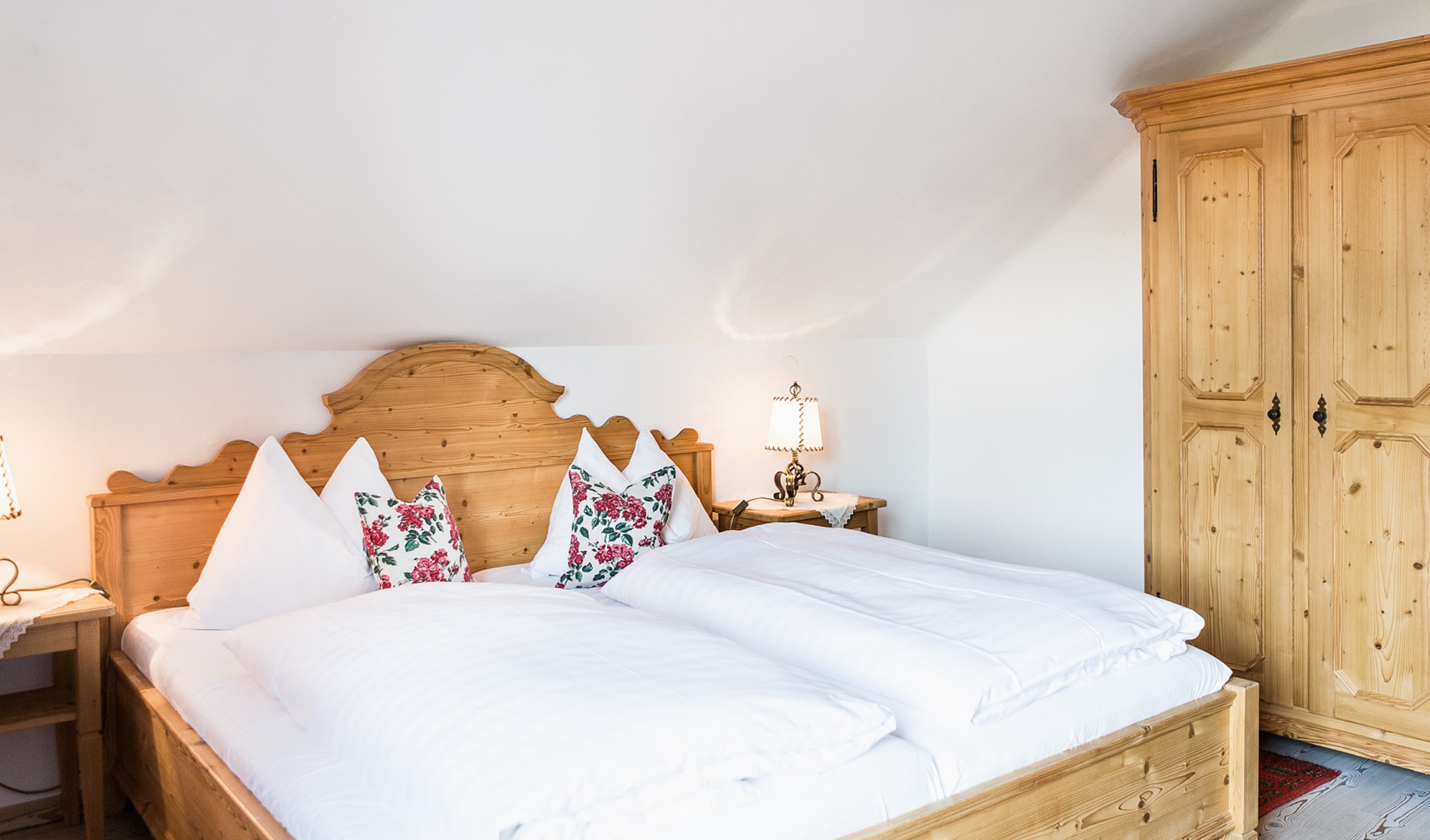 Rustikales Schlafzimmer aus Holz mit gemütlichem Doppelbett, floralen Kissen und passendem Kleiderschrank.