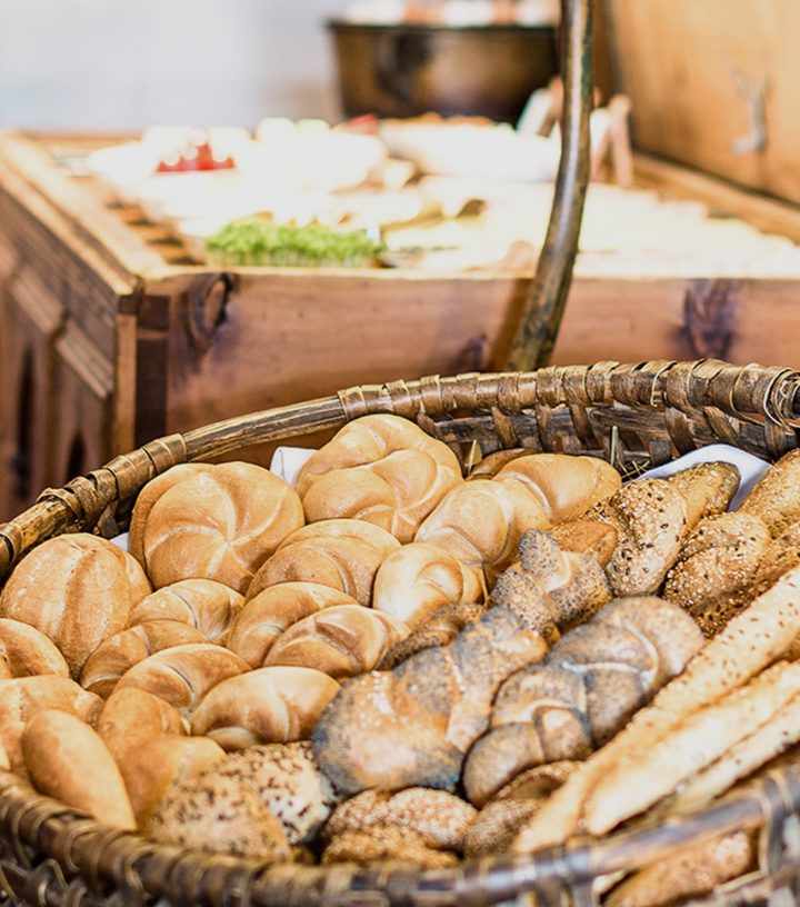 Korb voller frischer Brötchen, Kaisersemmeln und Mohngebäck auf einem Frühstücksbuffet.