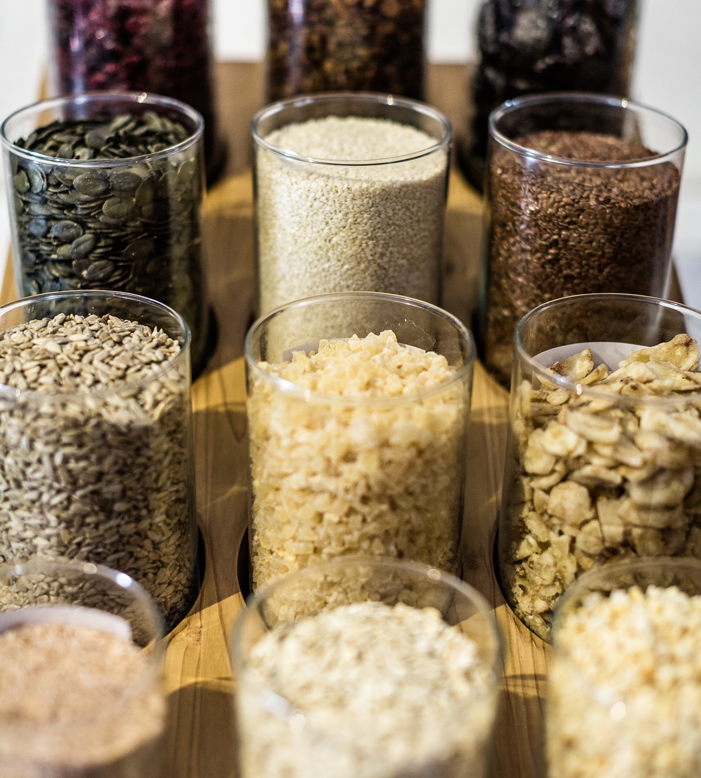 Gläser gefüllt mit verschiedenen Samen, Kernen und Müsli-Zutaten auf einem Holzständer.