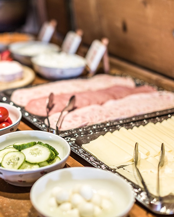 Frühstücksbuffet mit Wurst- und Käseplatten, Gurkenscheiben und Mozzarella in Schalen.