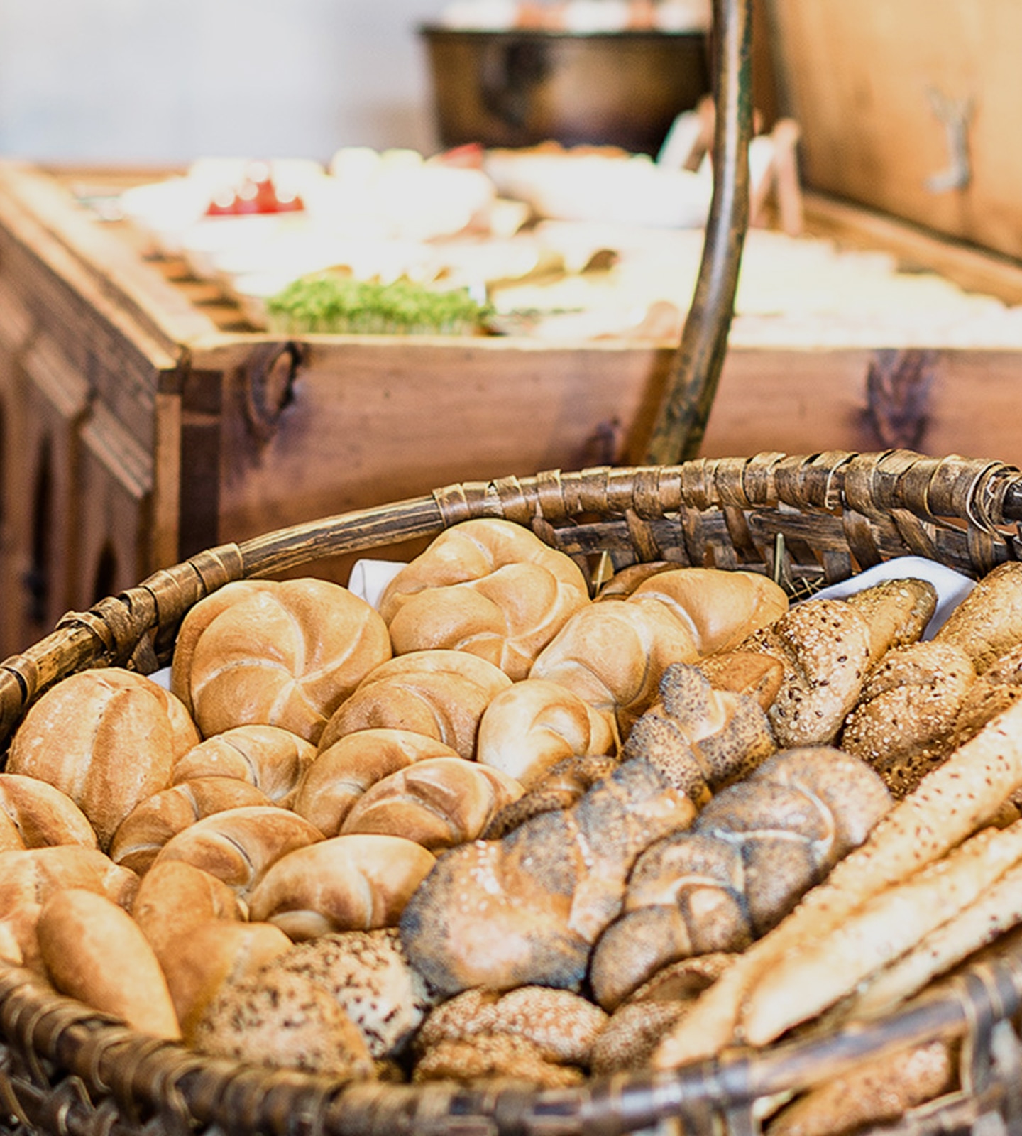 Ein geflochtener Korb voller frischer, verschiedener Brötchen auf einem Frühstücksbuffet.