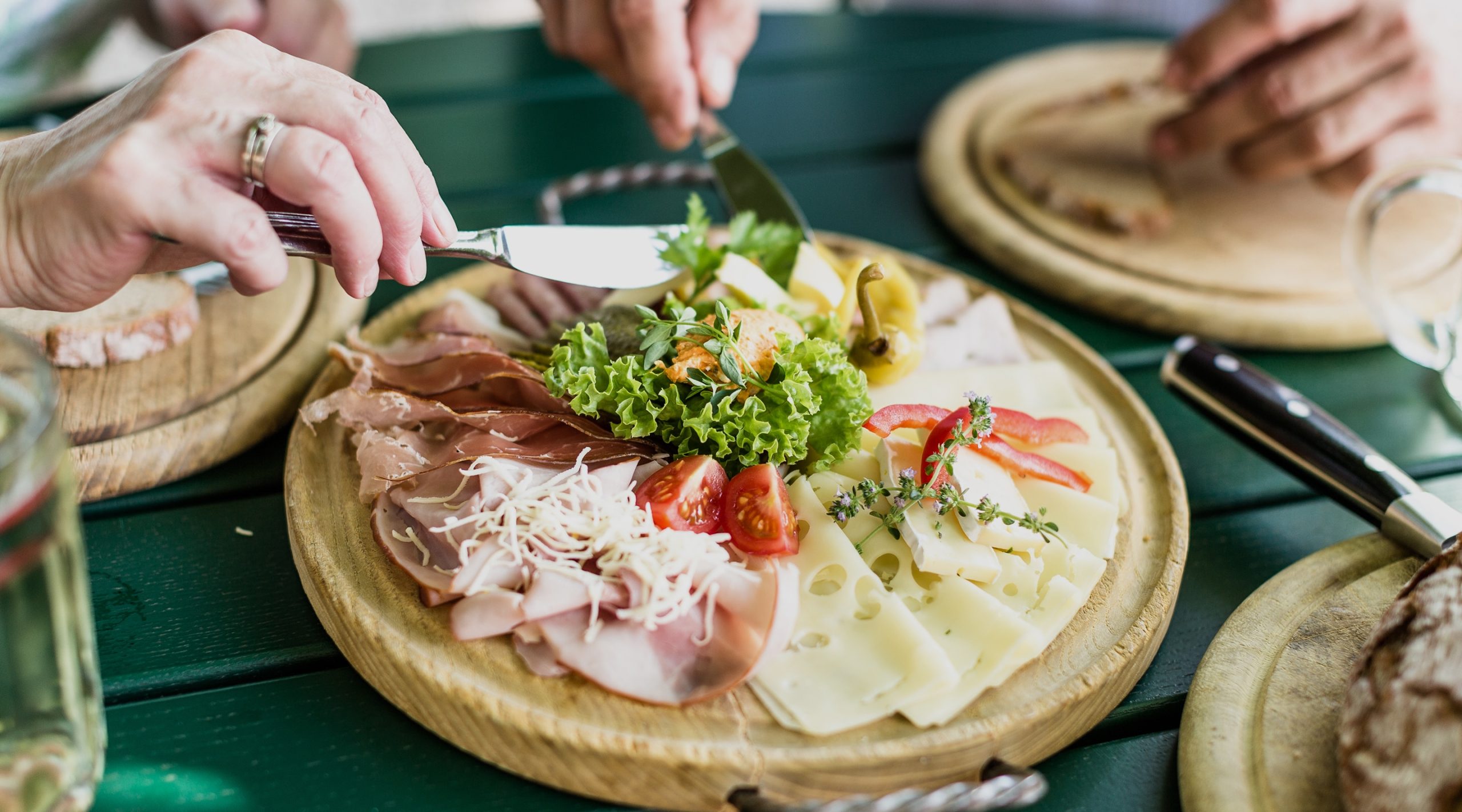 Nahaufnahme einer reichhaltigen Brettljause mit Schinken, Käse und Salat, serviert auf einem Holzteller.