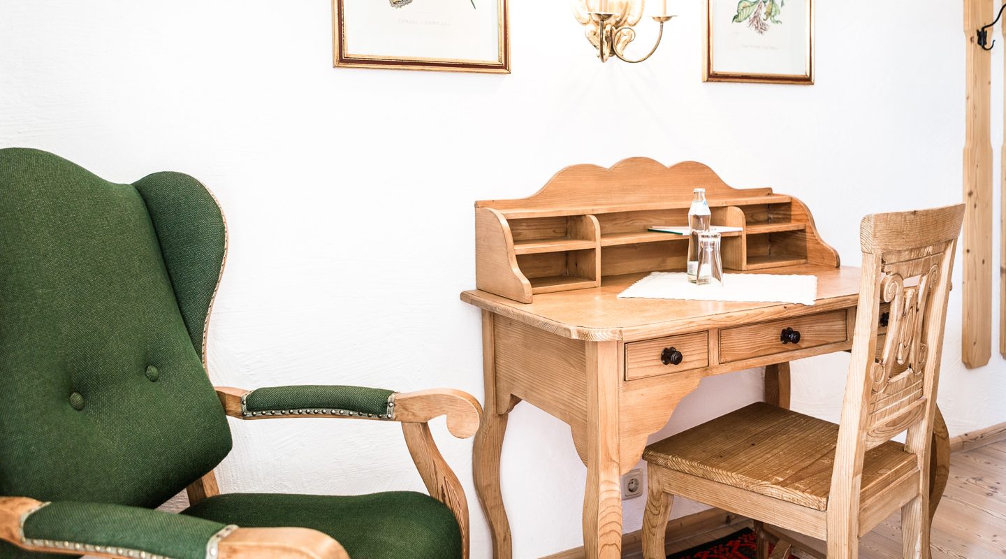 Rustikaler Holzschreibtisch mit passendem Stuhl neben einem grünen Sessel in einem Zimmer.