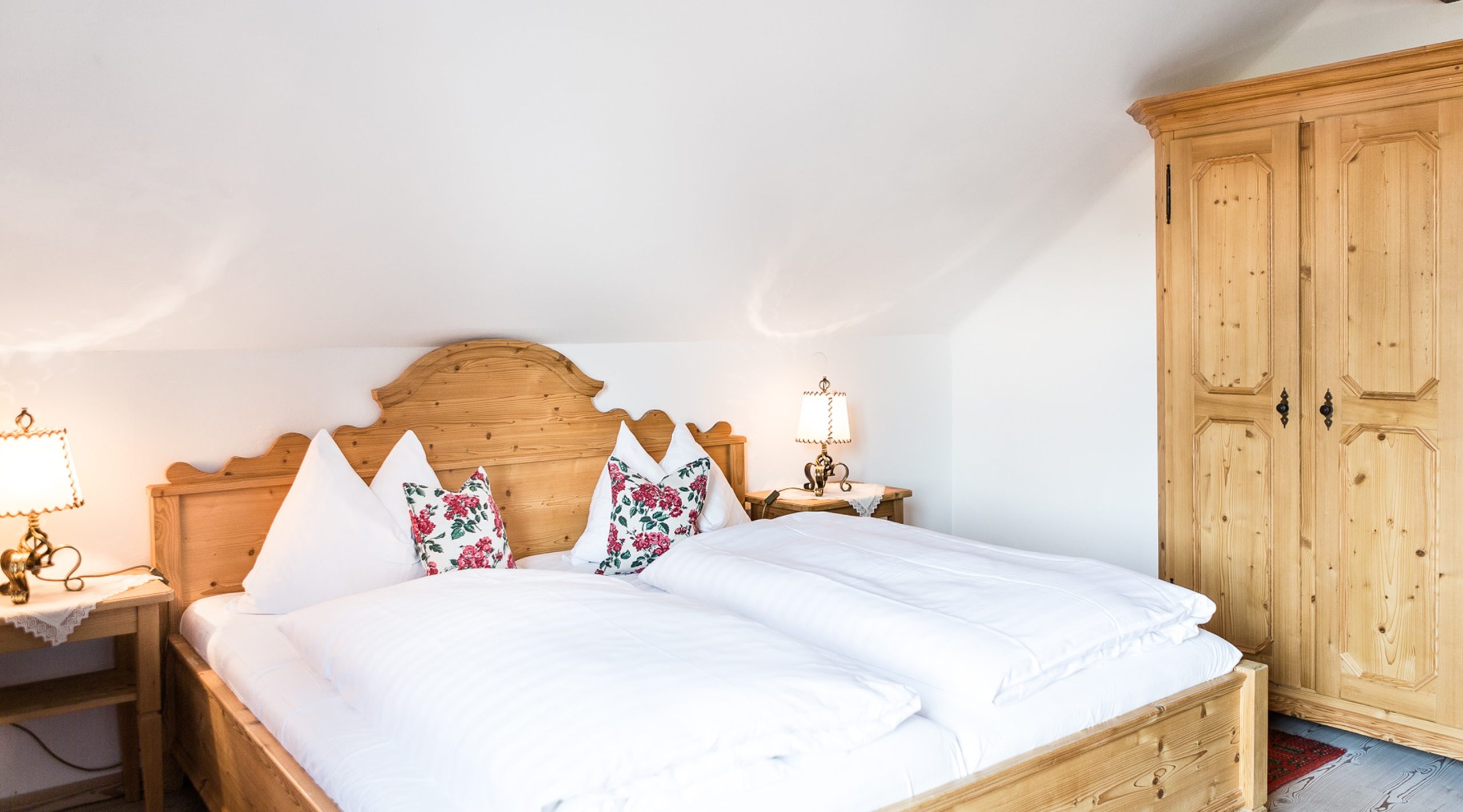 Rustikales Schlafzimmer im Landhausstil mit Holzbett, weißen Kissen und einem großen Kleiderschrank aus Holz.