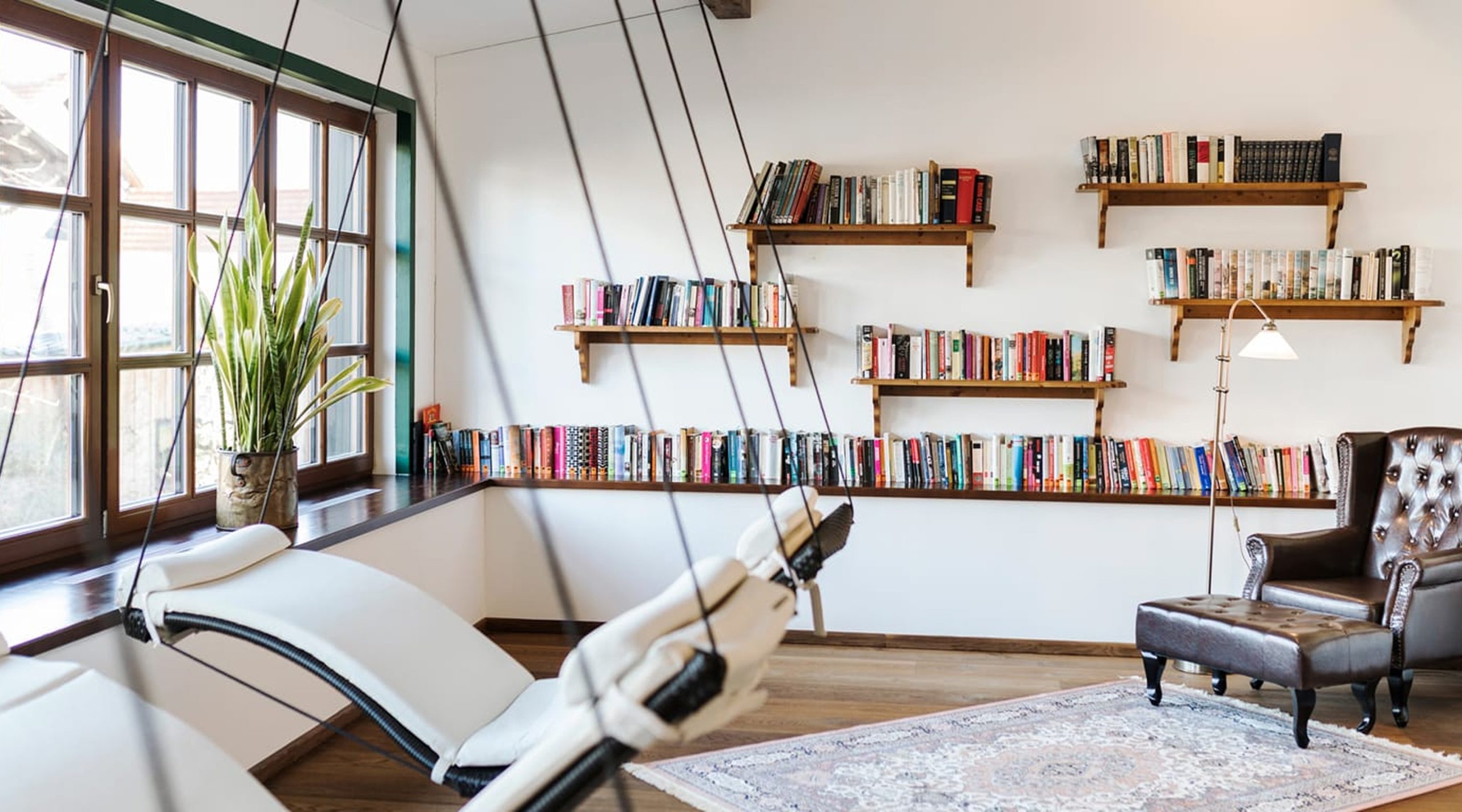Gemütlicher Leseraum mit Hängesesseln, Bücherregalen an der Wand und einem Ledersessel.