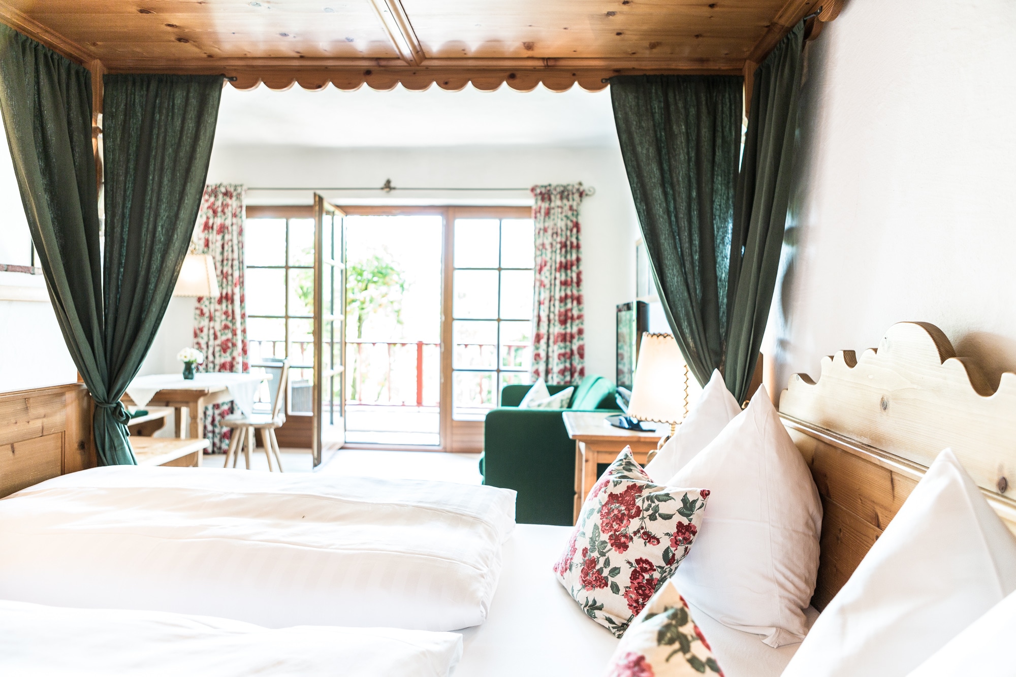 Gemütliches Hotelzimmer im Landhausstil mit Himmelbett aus Holz und Blick in den Wohnbereich mit Balkontür.