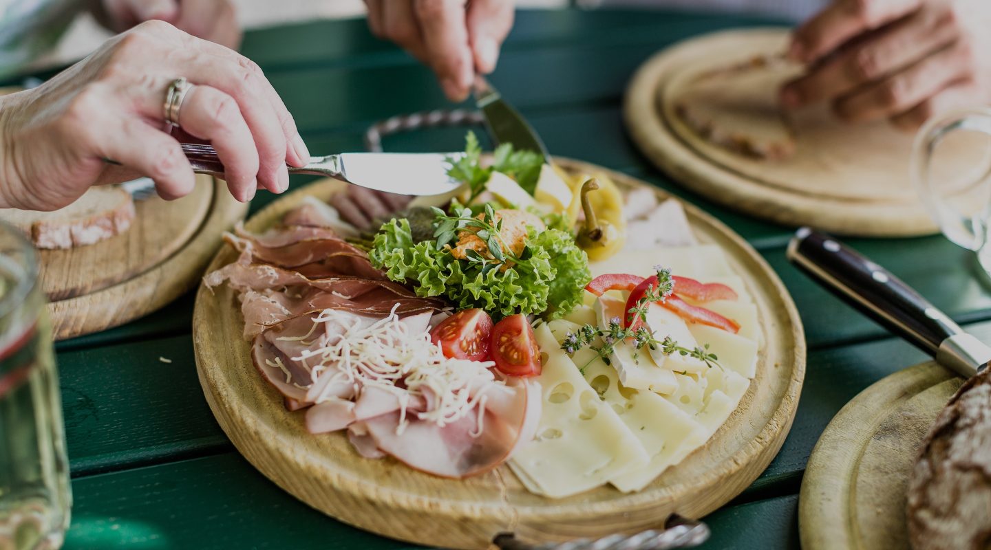 Nahaufnahme einer rustikalen Brotzeitplatte mit Käse, Schinken und Salat, serviert auf einem Holzteller.