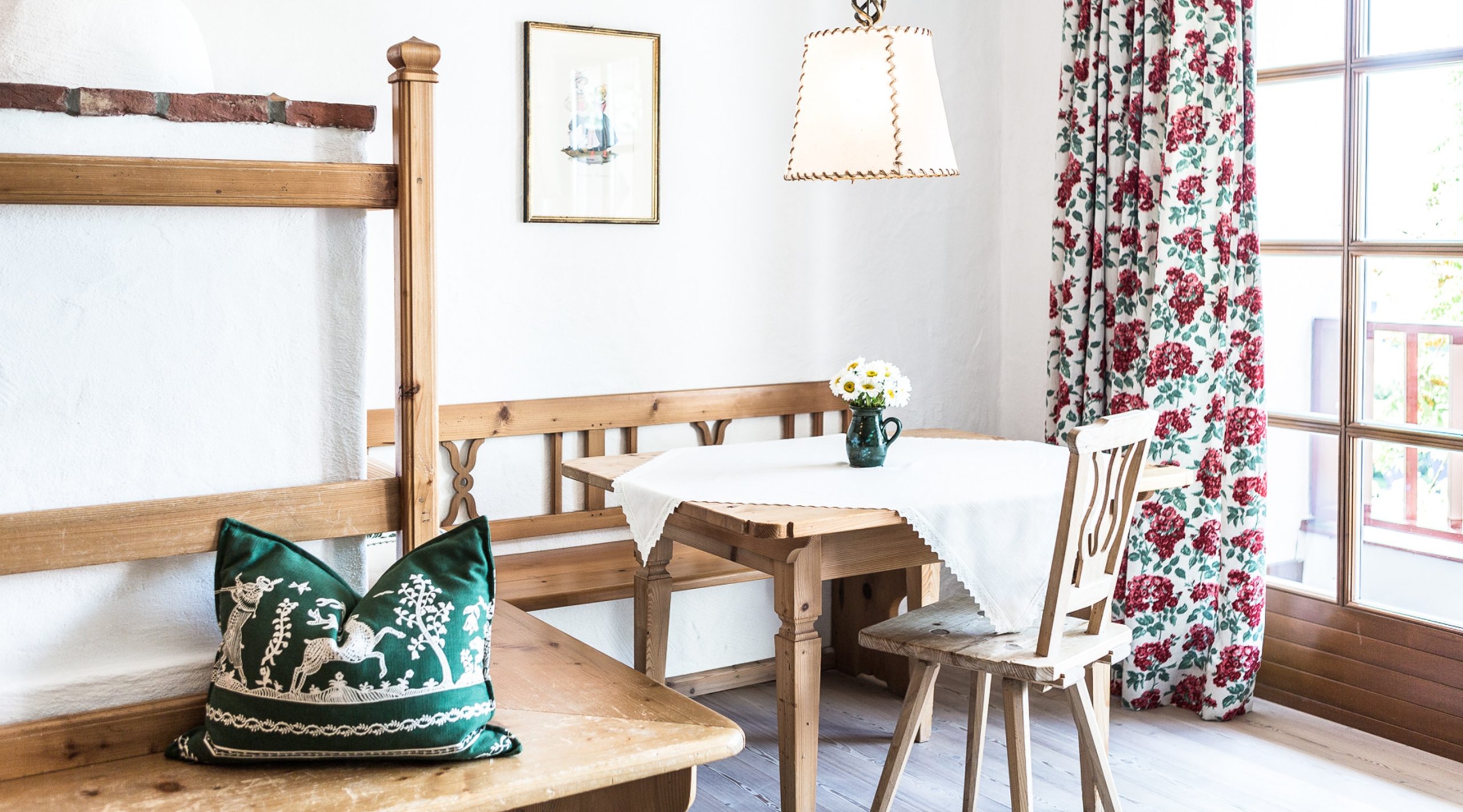 Rustikale Essecke aus Holz mit Eckbank, Tisch, grünem Kissen, besticktem Vorhang und Lampe im Landhausstil.