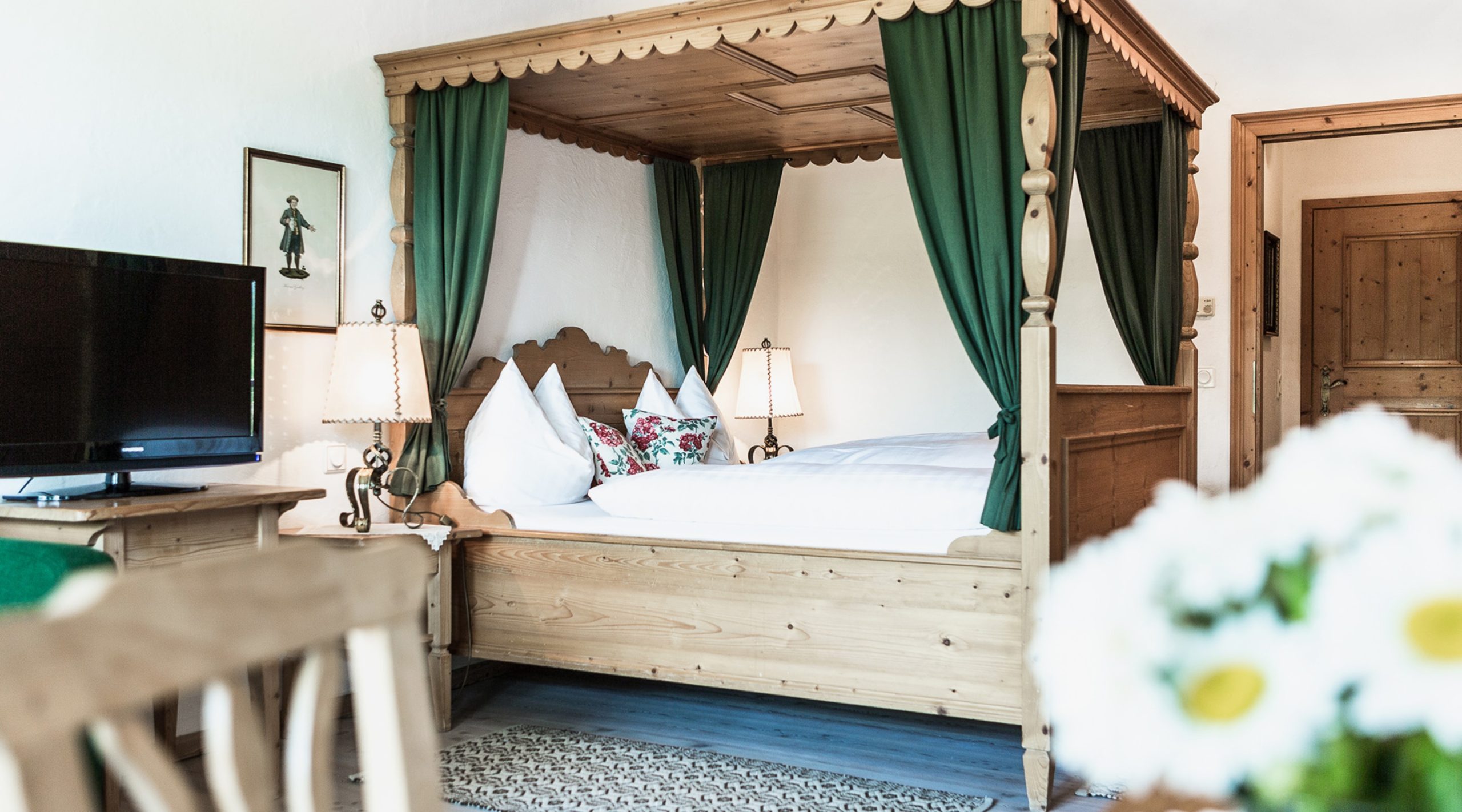 Rustikales Himmelbett aus Holz mit grünen Vorhängen und weißer Bettwäsche in einem gemütlichen Zimmer.