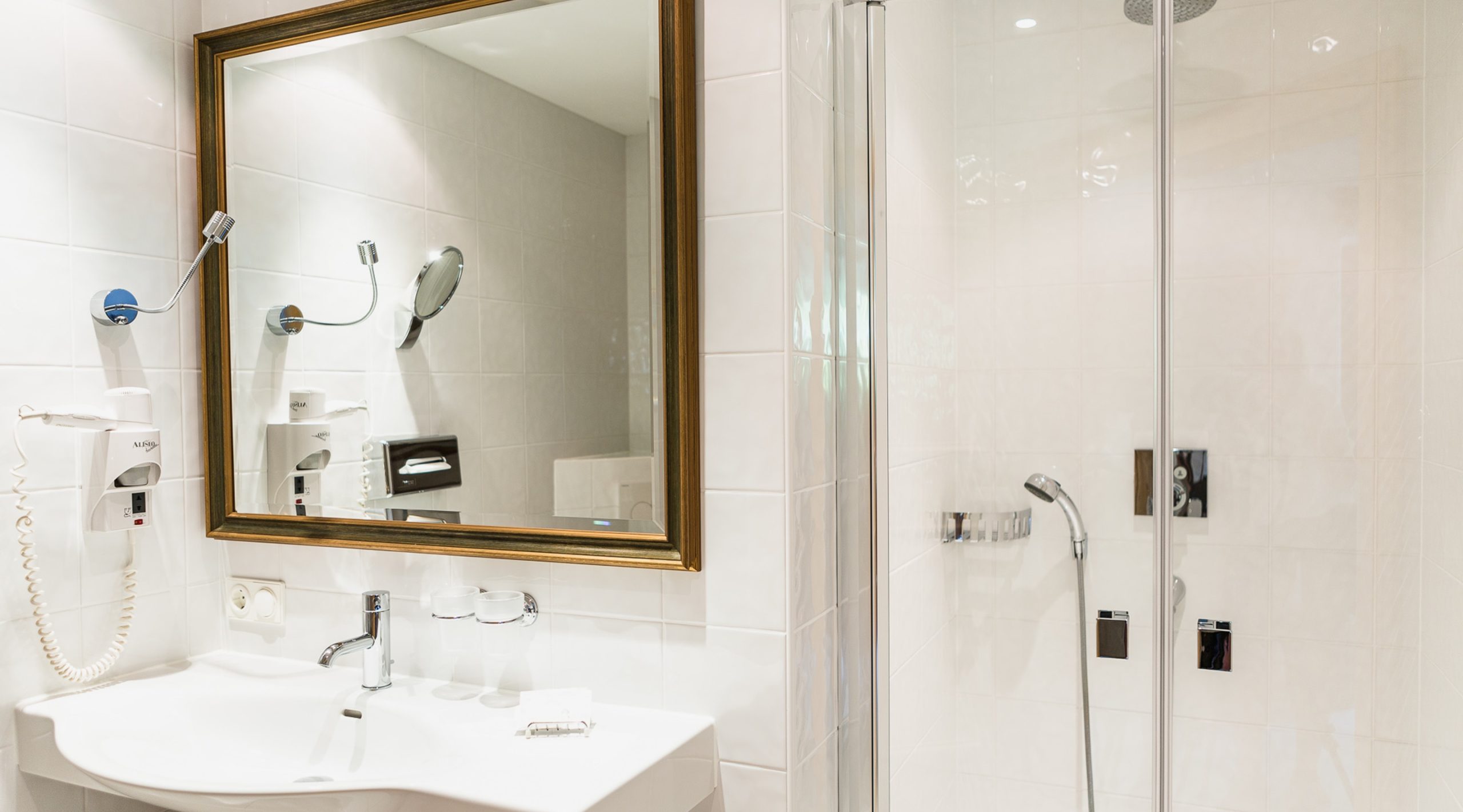 Modernes Badezimmer mit Waschbecken, großem Spiegel und einer verglasten Duschkabine mit weißen Fliesen.