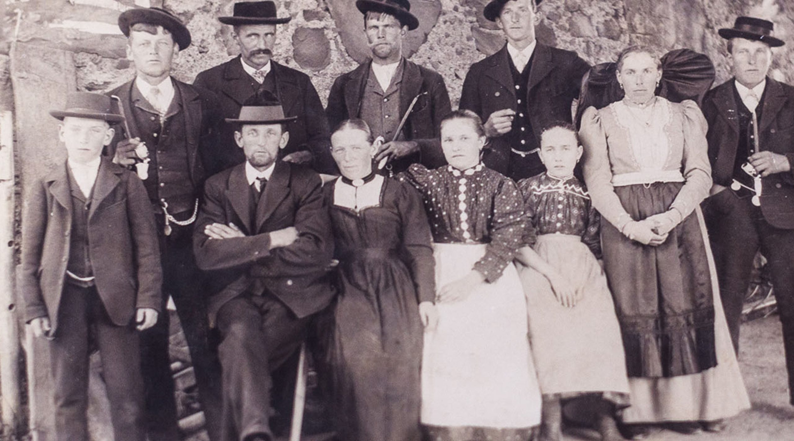 Historisches Gruppenfoto einer Familie in traditioneller deutscher Kleidung und Hüten vor einer Steinmauer.