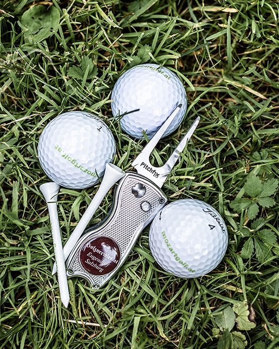 Drei Golfbälle, zwei Tees und ein Pitchfix-Werkzeug auf grünem Gras.