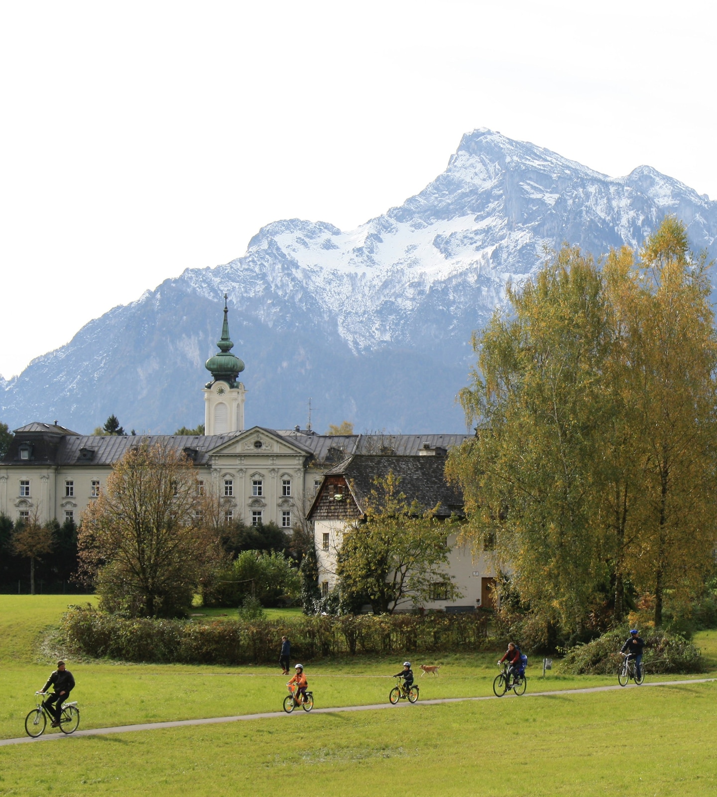 Radfahrer auf einem Weg vor dem Schloss Leopoldskron in Salzburg mit dem Untersberg im Hintergrund.