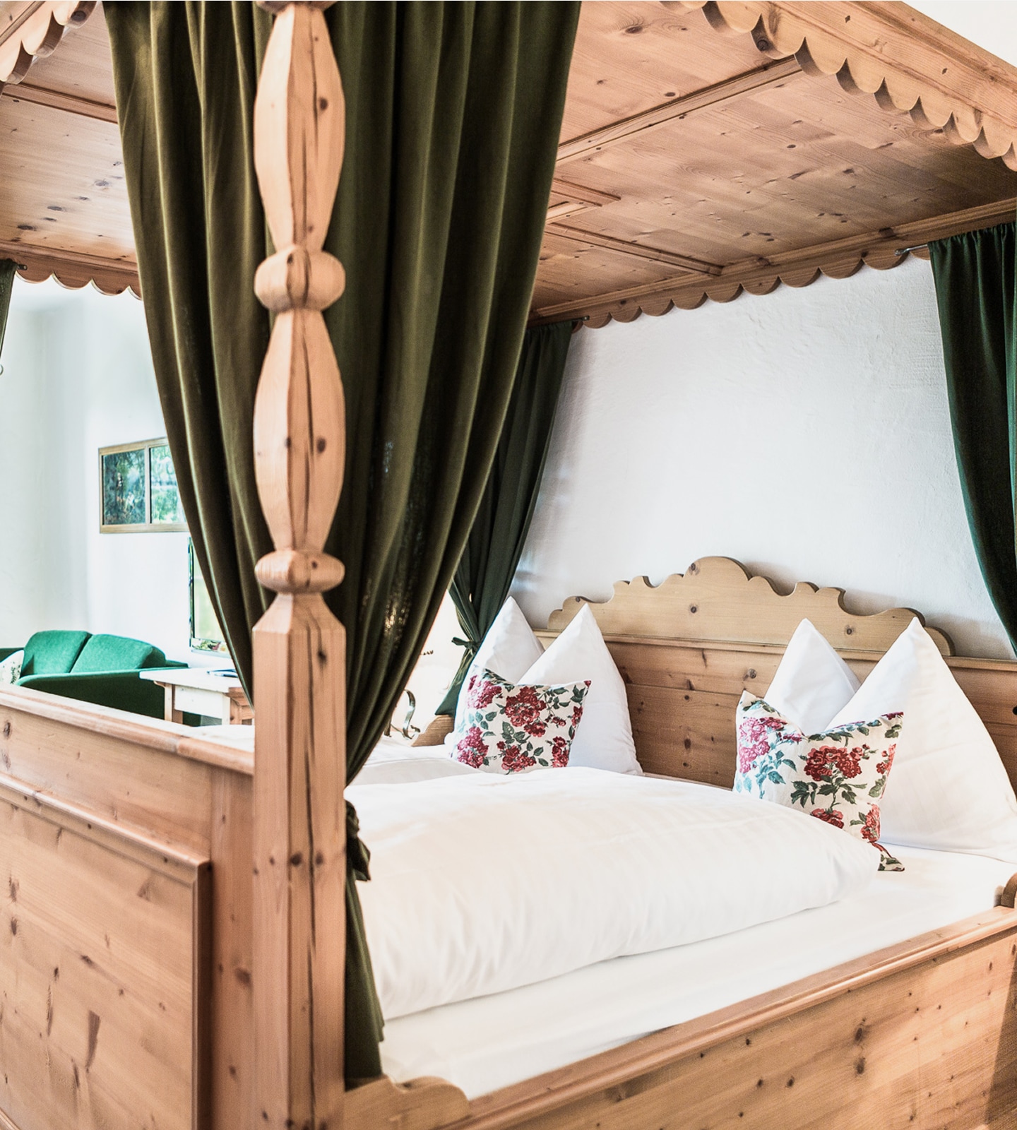 Rustikales Himmelbett aus Holz mit grünen Vorhängen und weißer Bettwäsche im alpinen Stil.