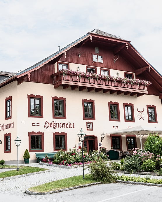 Das traditionelle Gasthaus Holznerwirt mit holzverziertem Balkon und blumengeschmücktem Vorgarten.
