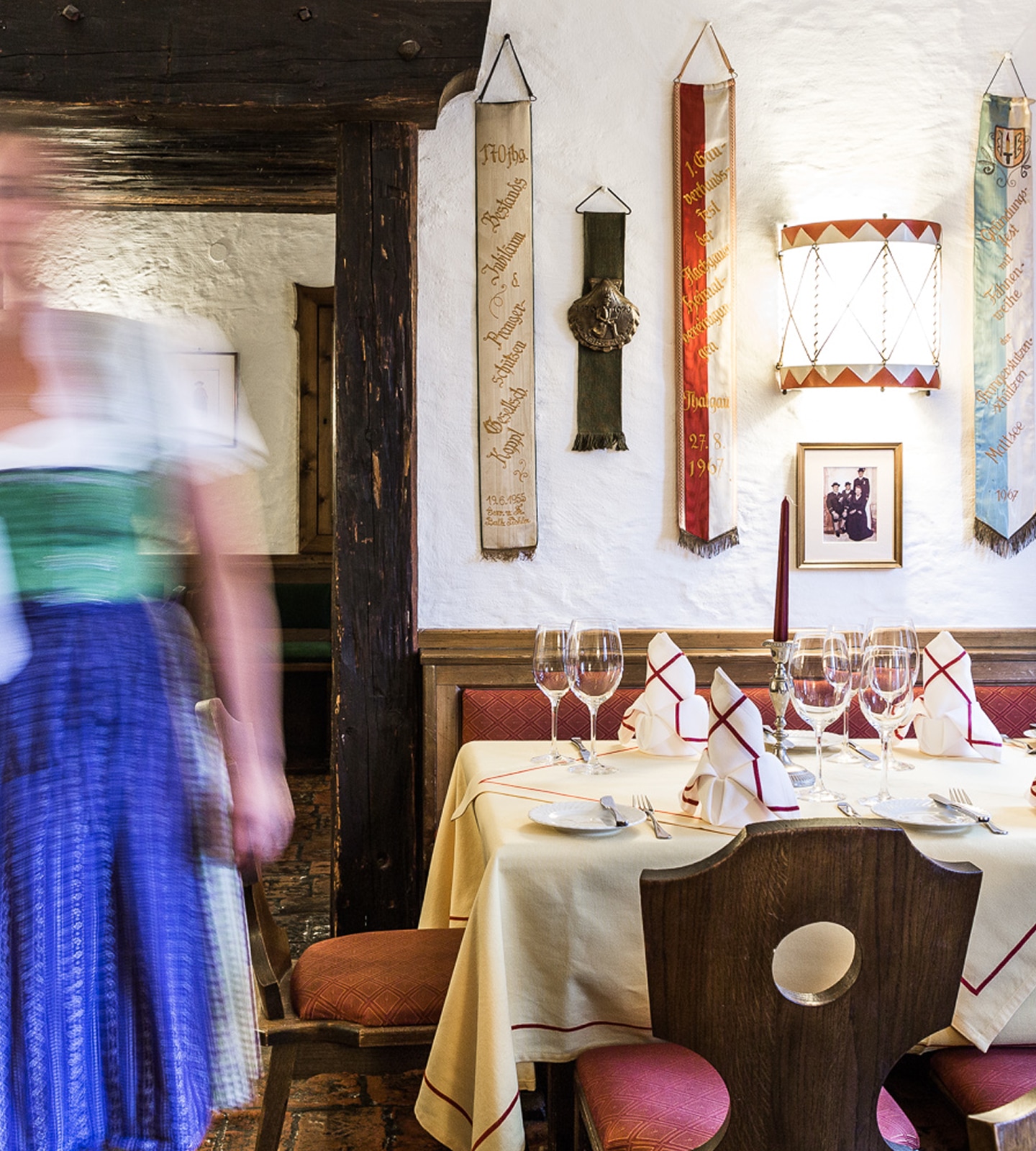Gedeckter Tisch im Gasthaus mit Wanddekor und einer unscharf vorbeigehenden Kellnerin im Dirndl.