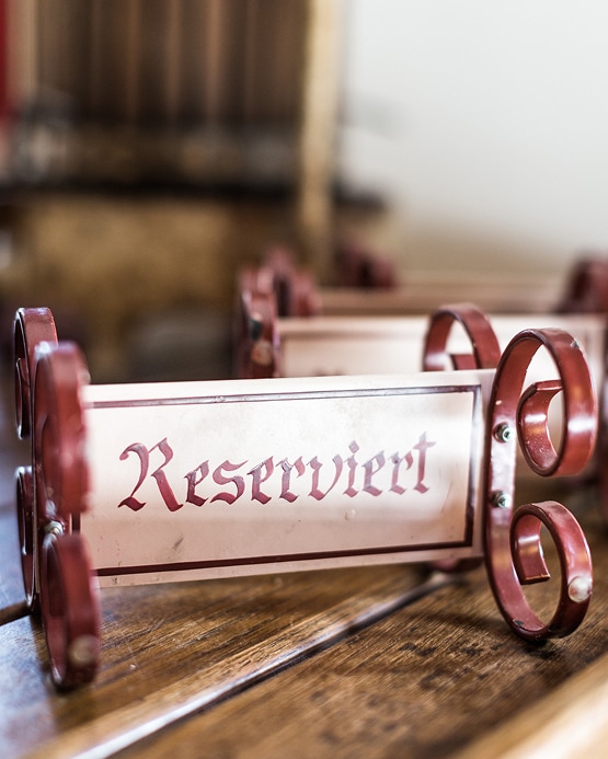 Ein antikes Tischaufstellerschild mit der roten Aufschrift „Reserviert“ in Altdeutscher Schrift auf einem Holztisch.