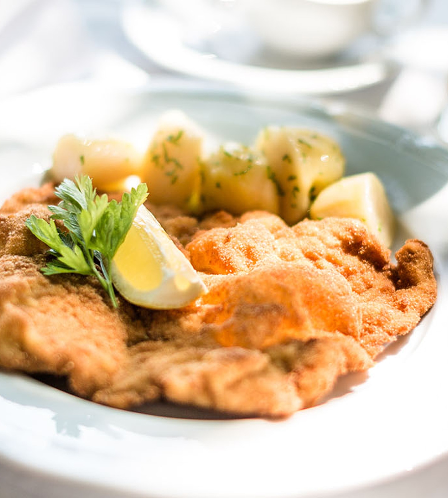 Knuspriges Wiener Schnitzel mit Petersilienkartoffeln, einer Zitronenspalte und Petersilie garniert.