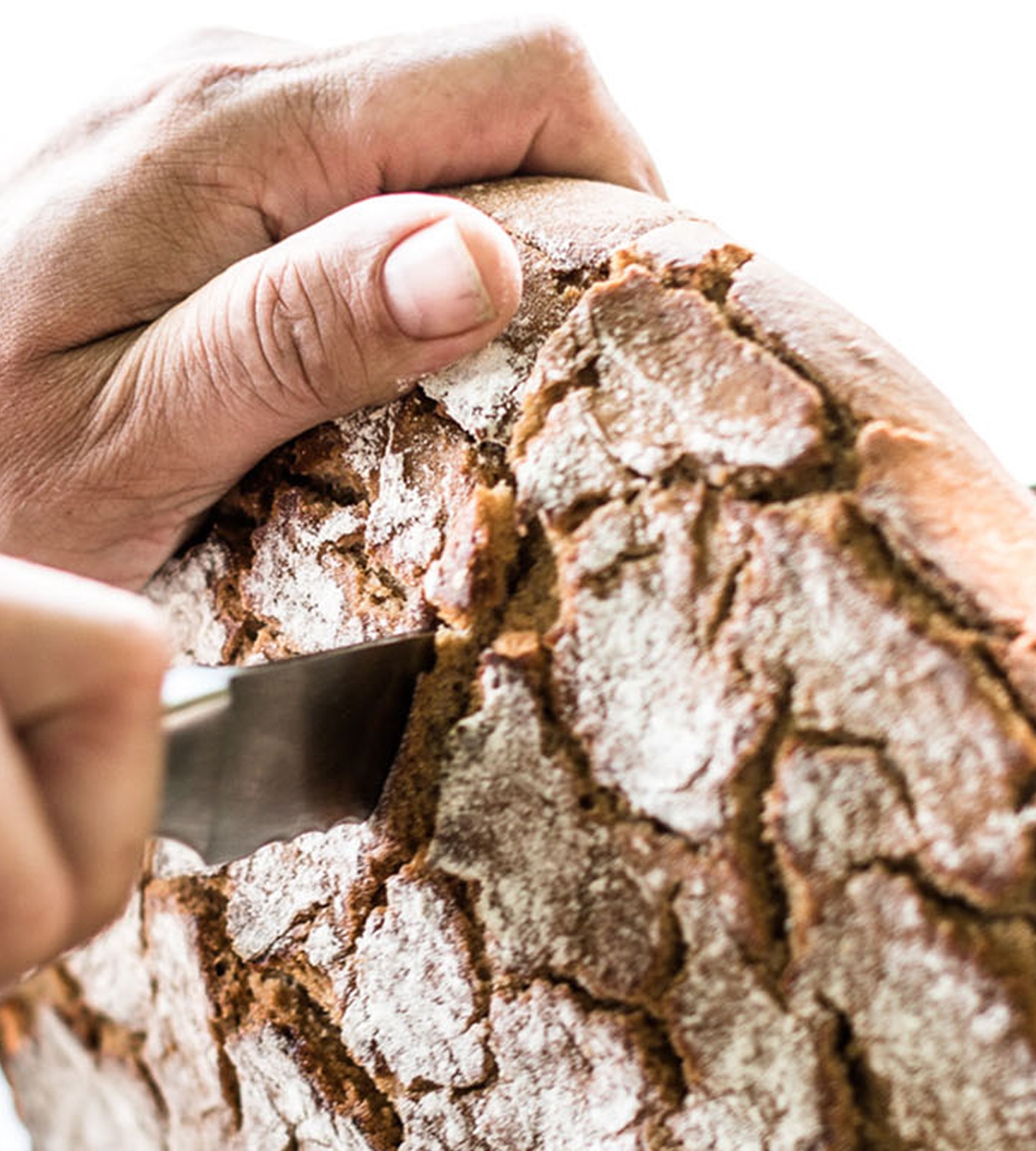 Hände schneiden mit einem Messer ein frisches, rustikales Bauernbrot mit bemehlter Kruste an.
