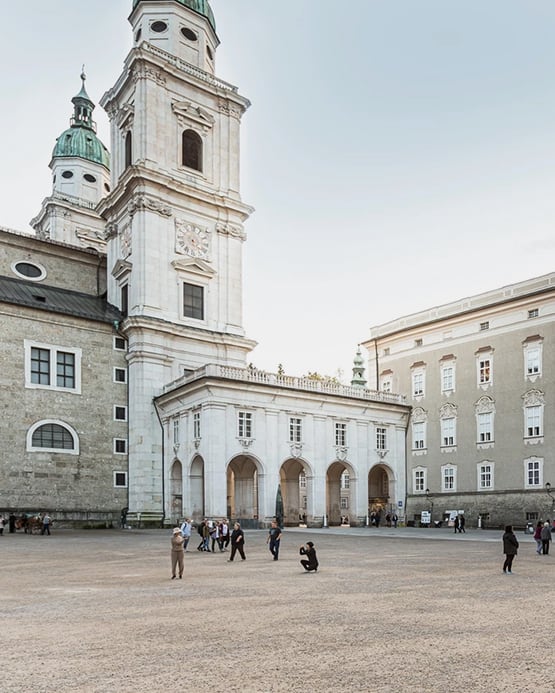 Blick auf den Salzburger Dom und den Domplatz mit Passanten bei Tageslicht.
