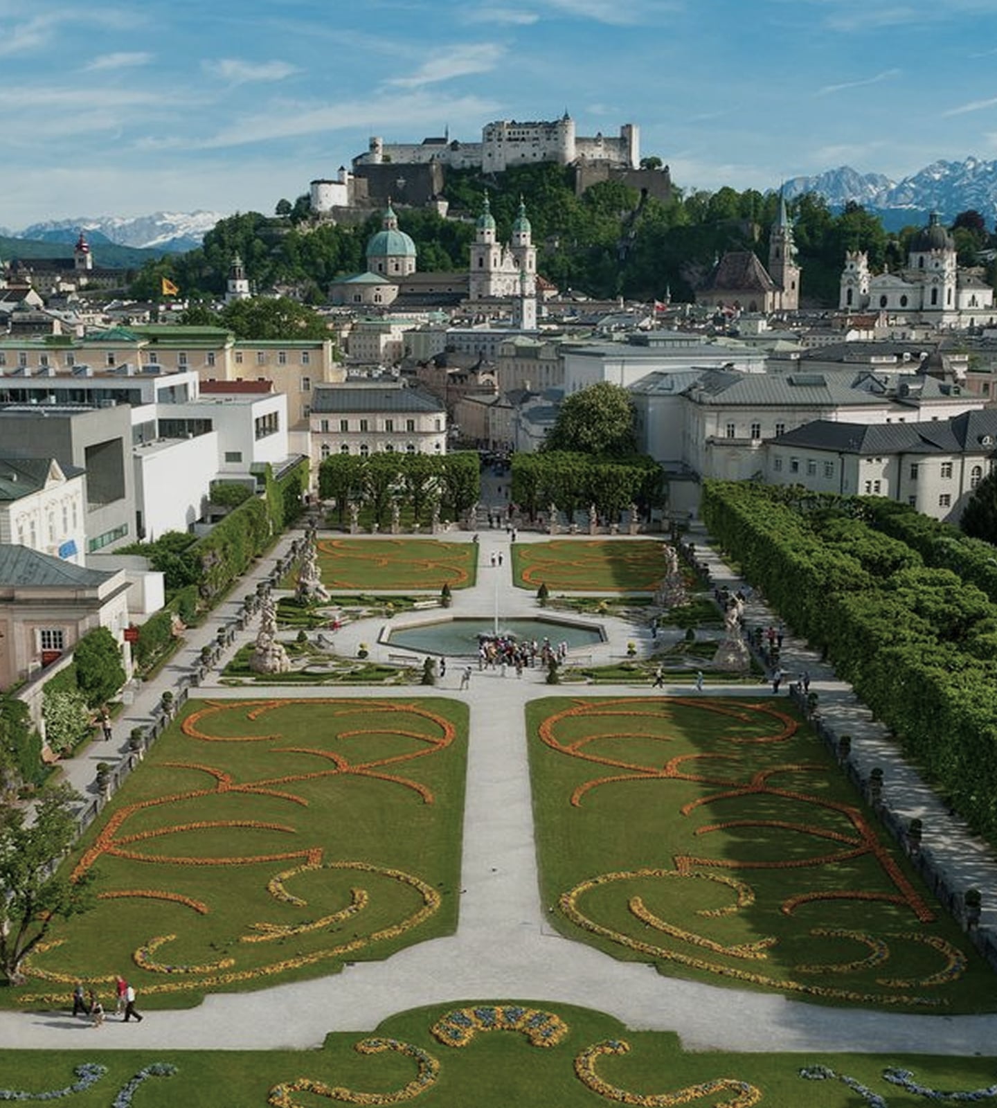 Blick über den Mirabellgarten in Salzburg auf die Festung Hohensalzburg unter blauem Himmel.