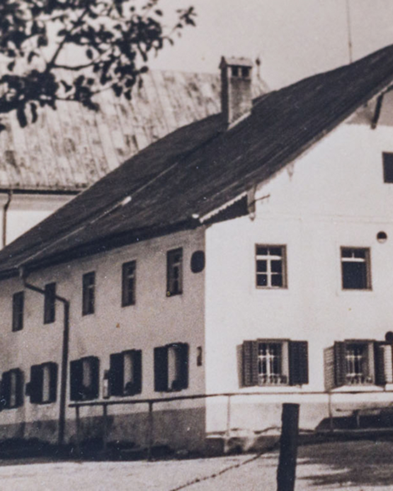 Historische Schwarz-Weiß-Aufnahme eines zweistöckigen Gebäudes mit Satteldach und Fensterläden.