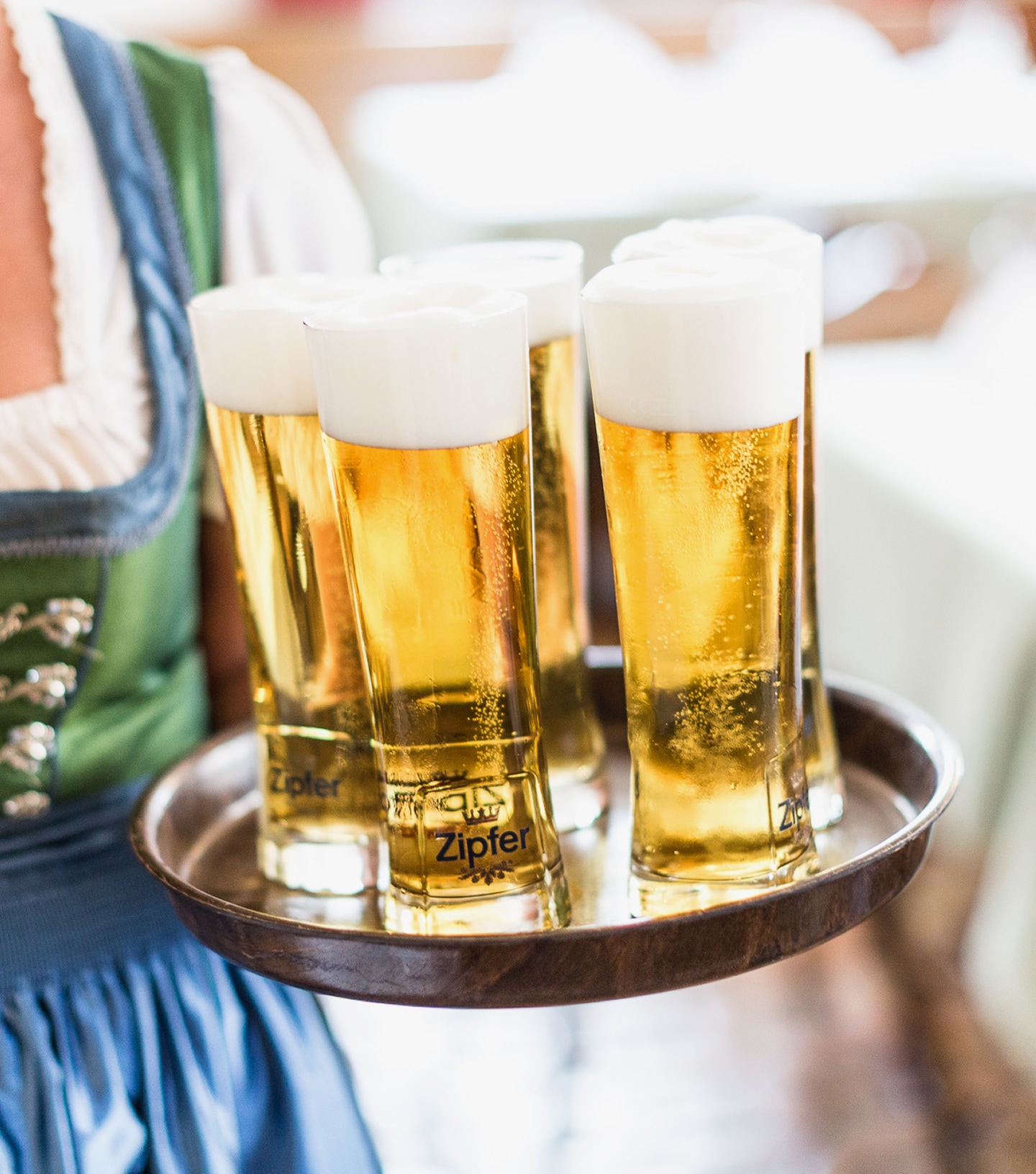 Eine Kellnerin im Dirndl serviert ein Tablett mit frisch gezapften Zipfer Biergläsern mit Schaumkrone.