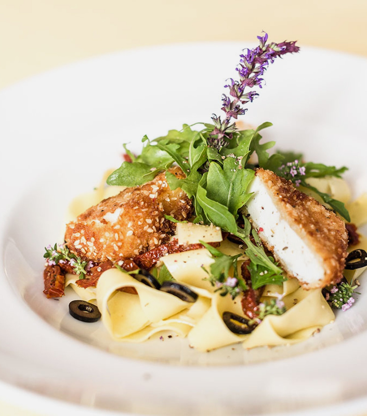 Tagliatelle mit paniertem Ziegenkäse, Oliven, getrockneten Tomaten und Rucola, garniert mit Lavendelblüte.