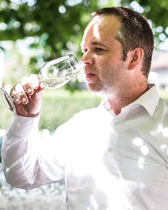 Ein Mann im weißen Hemd riecht an einem Glas Weißwein im Freien.