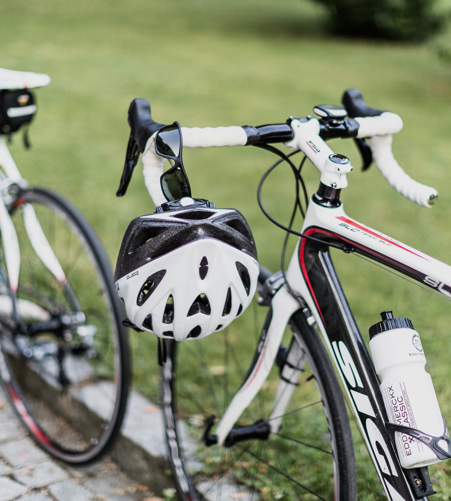 Rennrad mit weißem Helm und Sonnenbrille am Lenker, davor eine Trinkflasche im Halter.