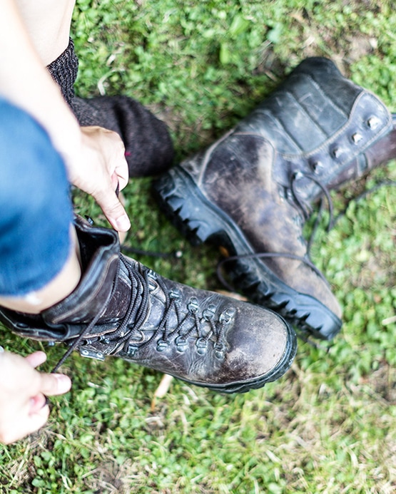 Eine Person schnürt ihre braunen Leder-Wanderschuhe auf einer grünen Wiese.