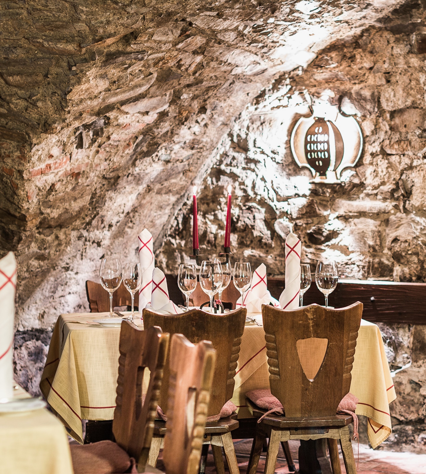 Festlich gedeckter Tisch in einem urigen Steinkeller mit Kerzenständern und Holzstühlen.