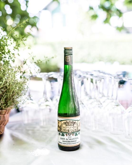 Eine Flasche Ried Achleiten Grüner Veltliner Weißwein steht vor vielen Weingläsern im Freien.
