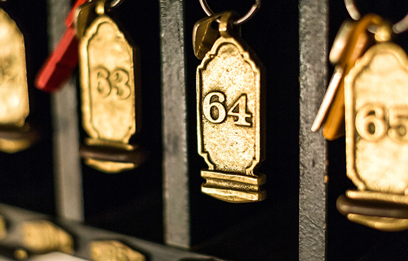 Antike goldene Zimmerschlüssel mit den Nummern 63, 64 und 65 hängen an einem Schlüsselbrett.