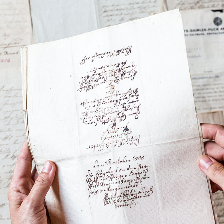 Zwei Hände halten ein historisches Dokument mit altdeutscher Schreibschrift, datiert auf den 15. Oktober 1800.