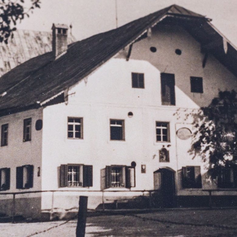 Historische Schwarz-Weiß-Aufnahme eines alten Bauernhauses im alpinen Stil mit Satteldach.