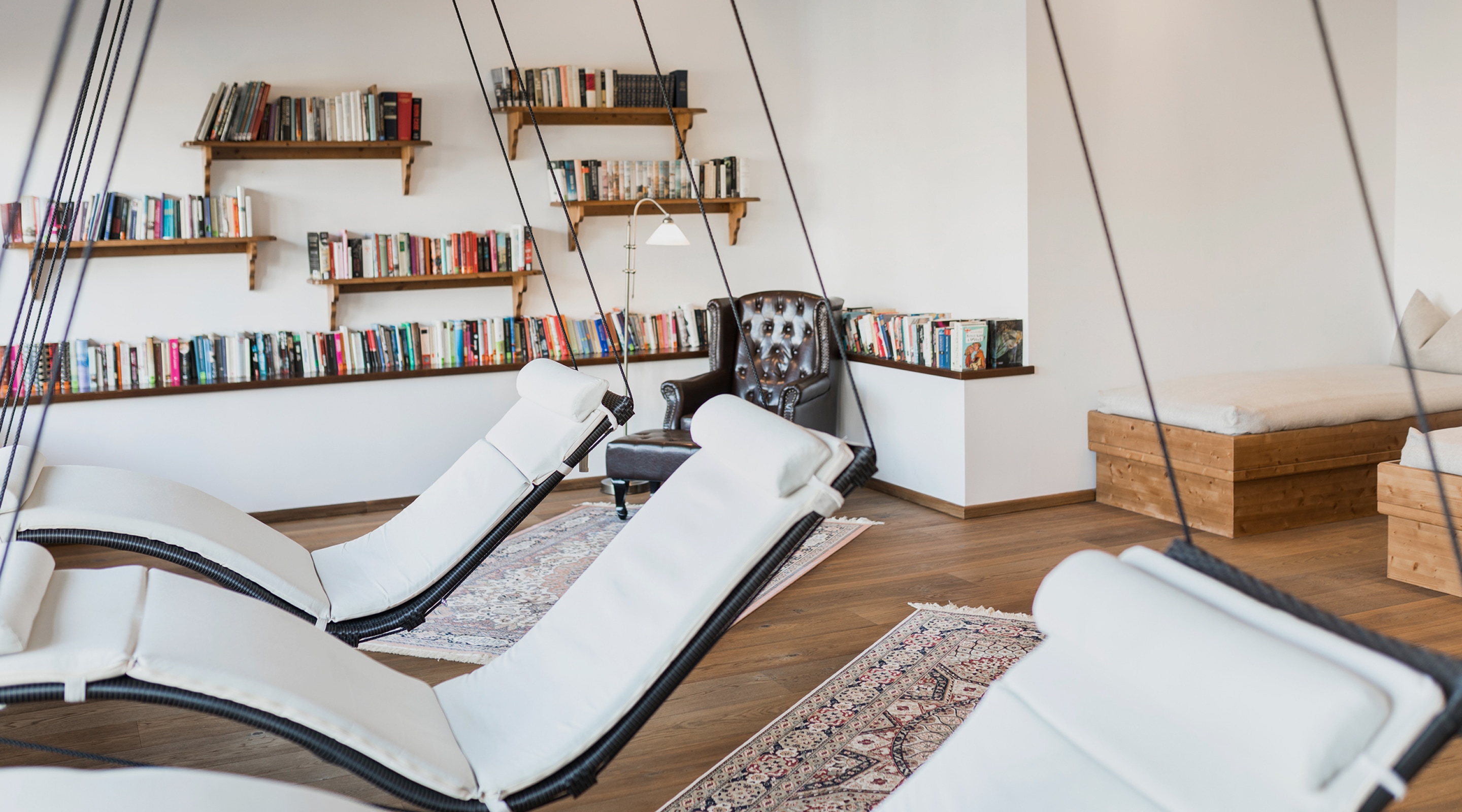 Gemütlicher Ruheraum mit schwebenden weißen Liegen, Holzboden und Bücherregalen an der Wand.