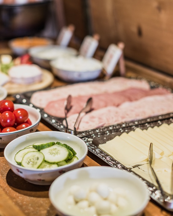 Breakfast buffet spread with bowls of cucumbers, tomatoes, and plates of sliced deli meats and cheeses.